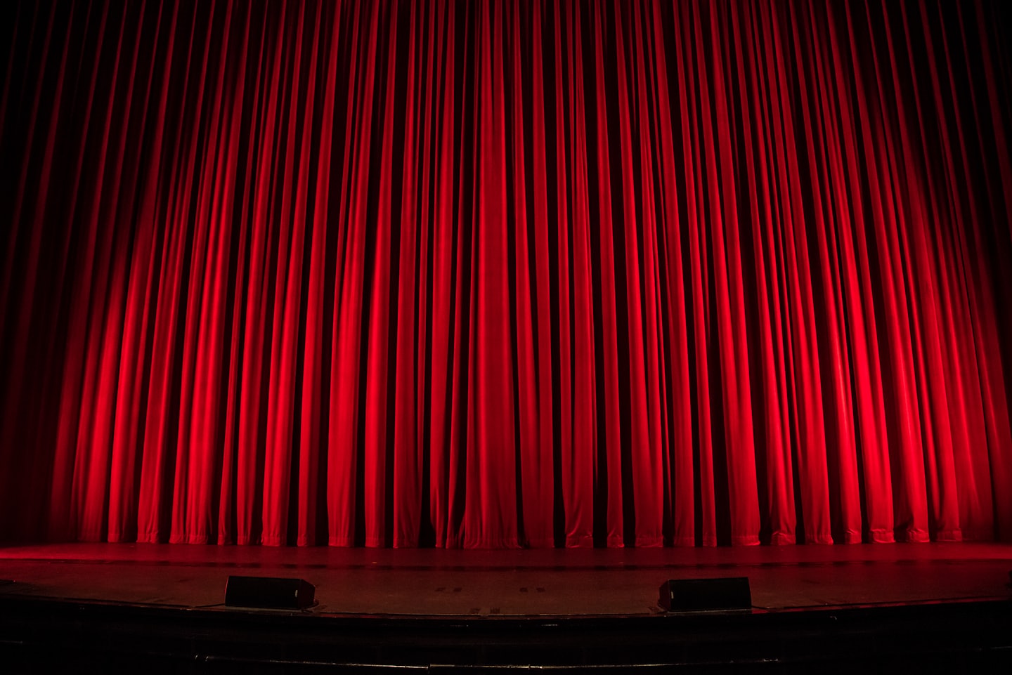A red stage curtain, closed and lit from above, on an empty stage