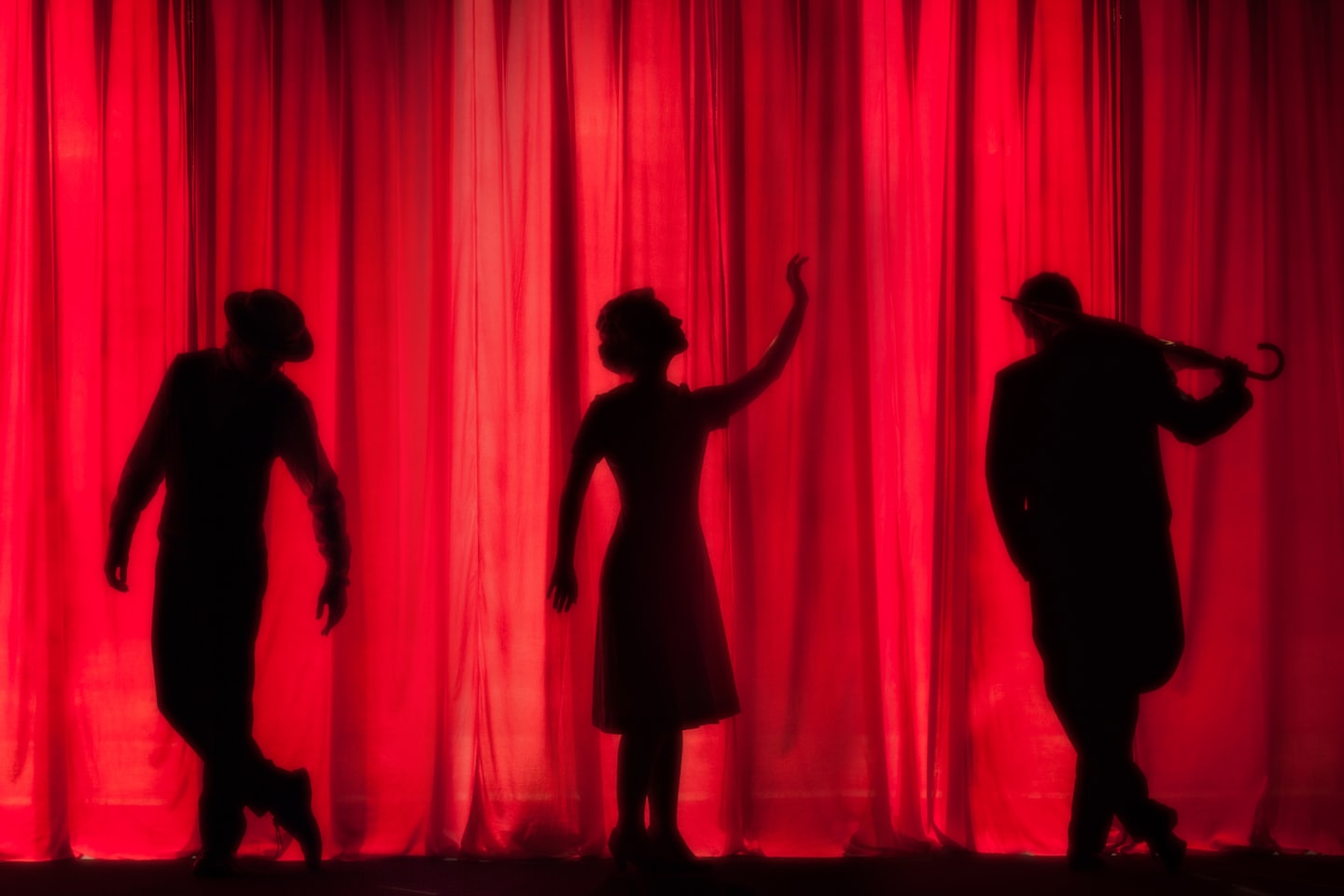 Silhouettes of three performers against a lit red stage curtain